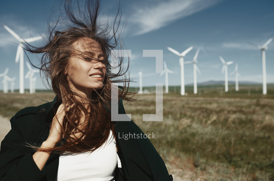 woman with hair blowing standing in a front of a wind farm