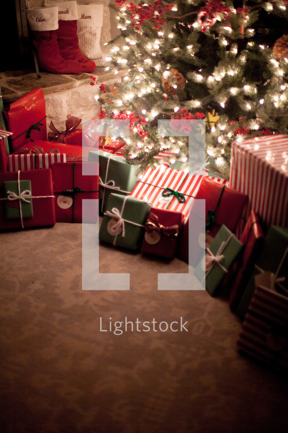 Gifts under a Christmas tree and stockings by a fireplace 