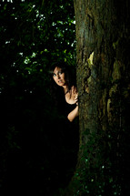 fearful woman peeking from behind a tree