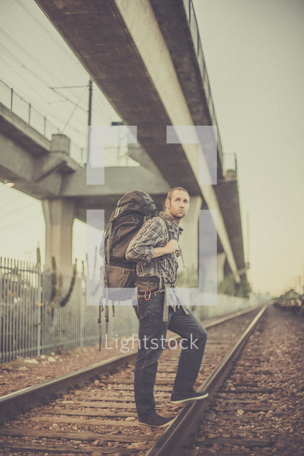 man backpacking standing on train tracks