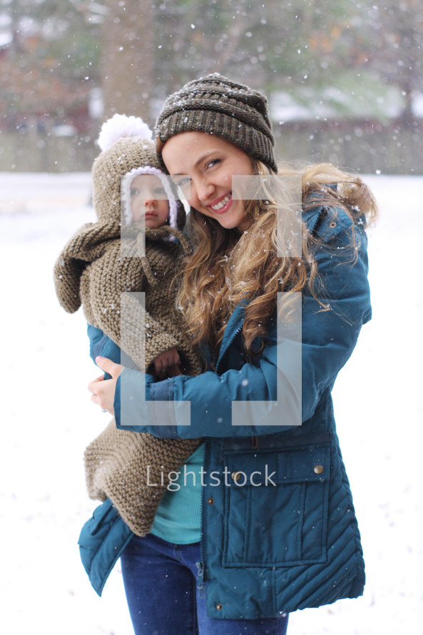 a mother holding a baby under falling snow 