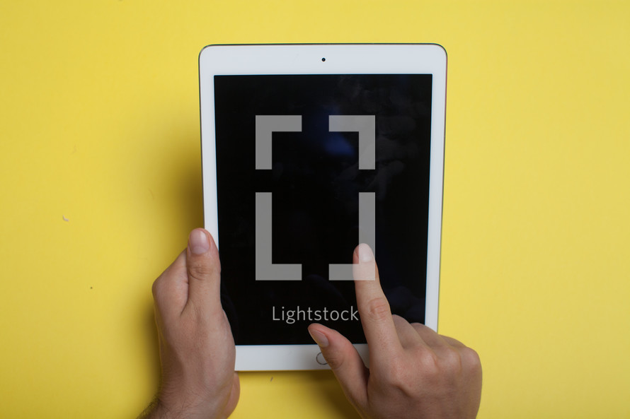 Hands holding an electronic tablet on a yellow background.