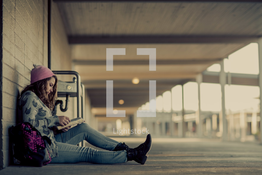 Teenage girl back to school studying, ready bible, campus, alone in a school hallway, wall, devotional