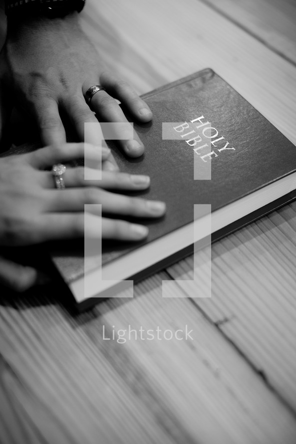 Husband and wife's hands on a Bible.