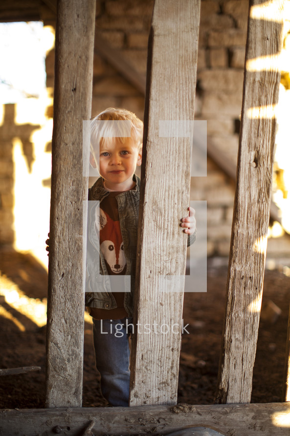 A toddler boy looking through the pickets of a fence. 