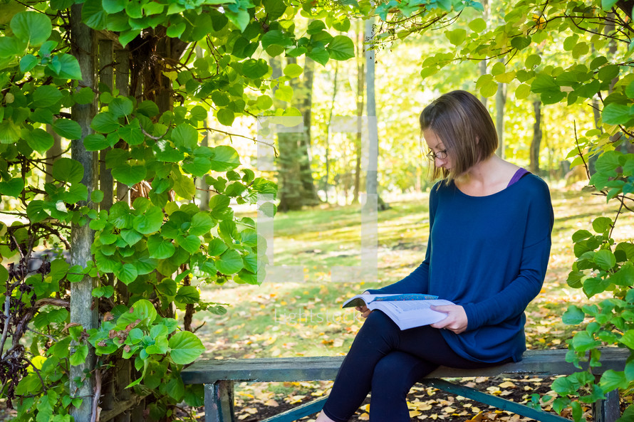 a woman sitting on a bench outdoors reading a Bible 