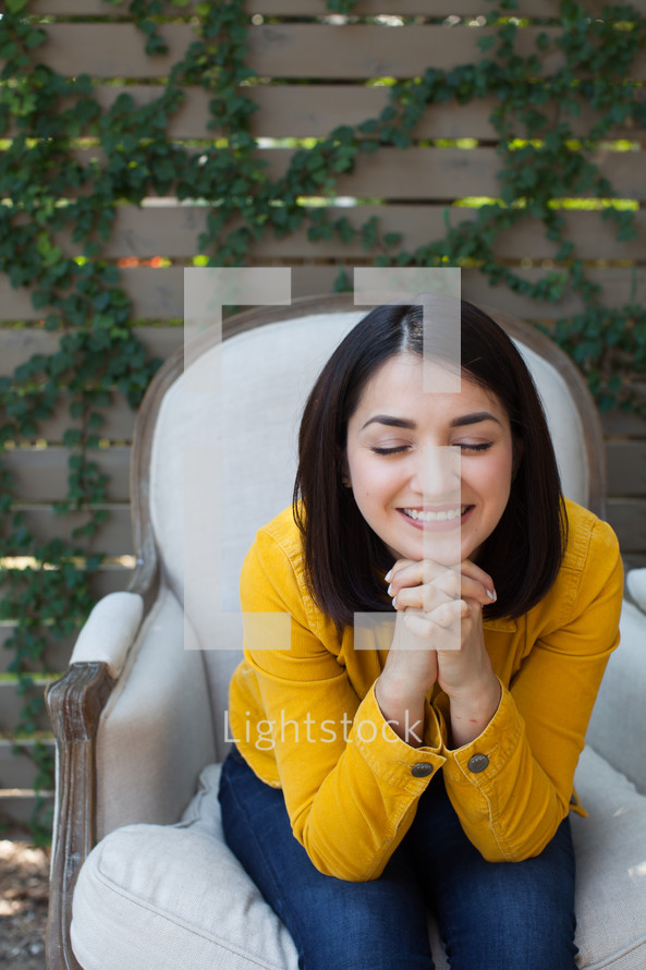 a woman sitting in a chair outdoors with praying hands 