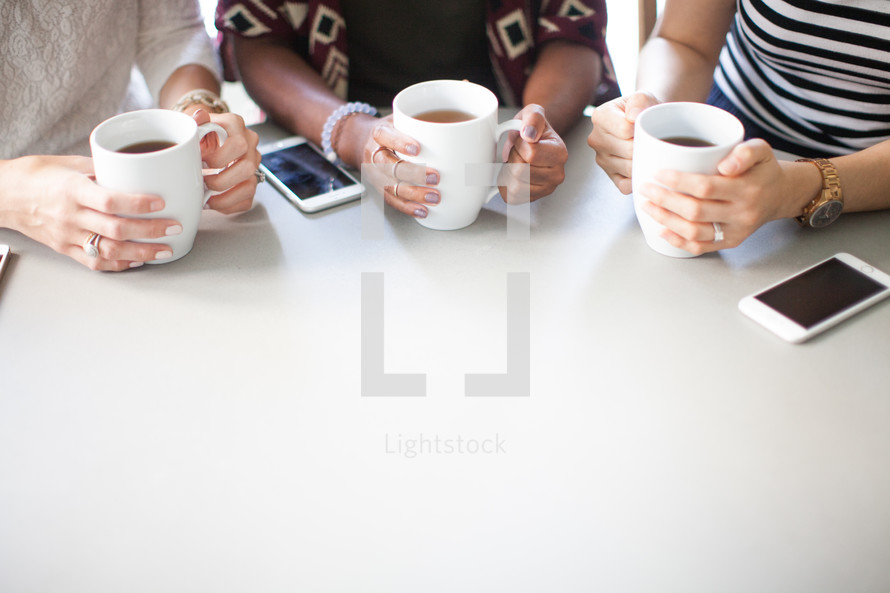 Three people sitting at a table with cell phones and coffee cups.