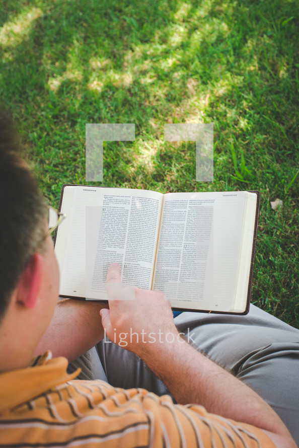 a man sitting in the grass reading a Bible 