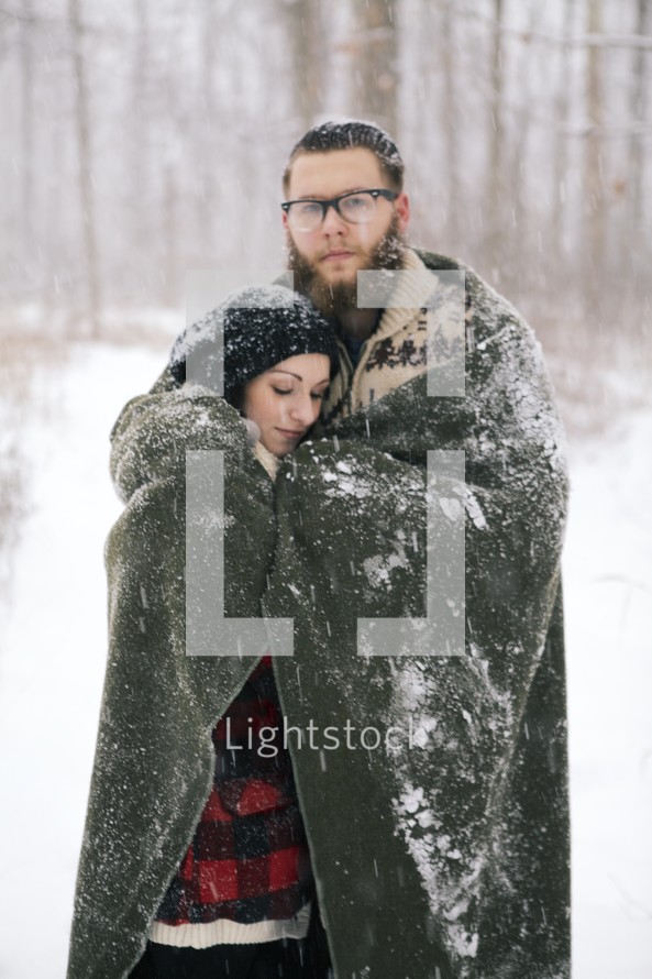 a couple hugging under a blanket in the snow 