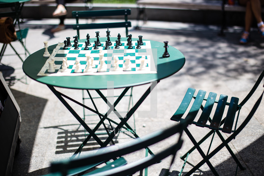 Chess set on a round table with a folding chair outside.