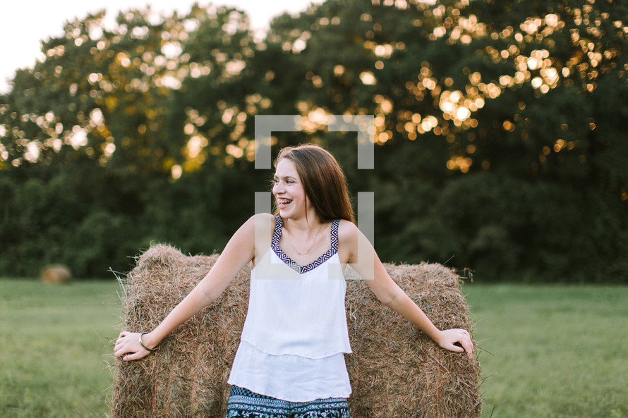 a young woman standing in front of a hay bale 
