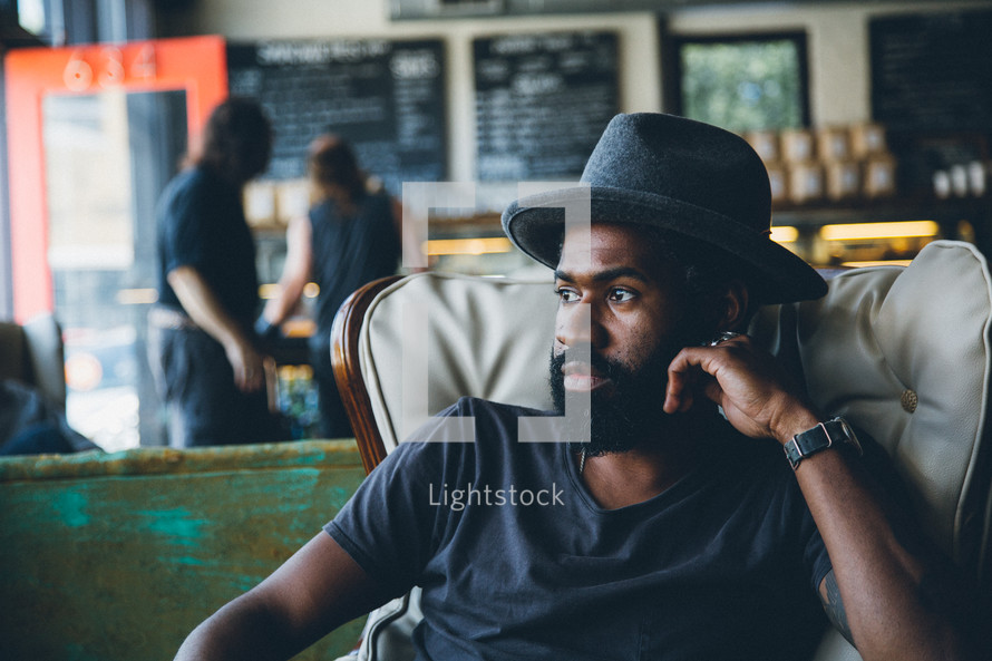 African American man sitting in a chair in a coffee shop thinking 