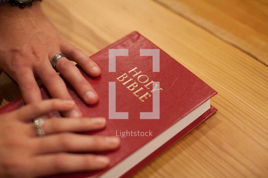 Hands of a husband and wife on a red Bible.