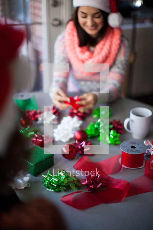 A woman in a santa hat smiling and wrapping Christmas presents