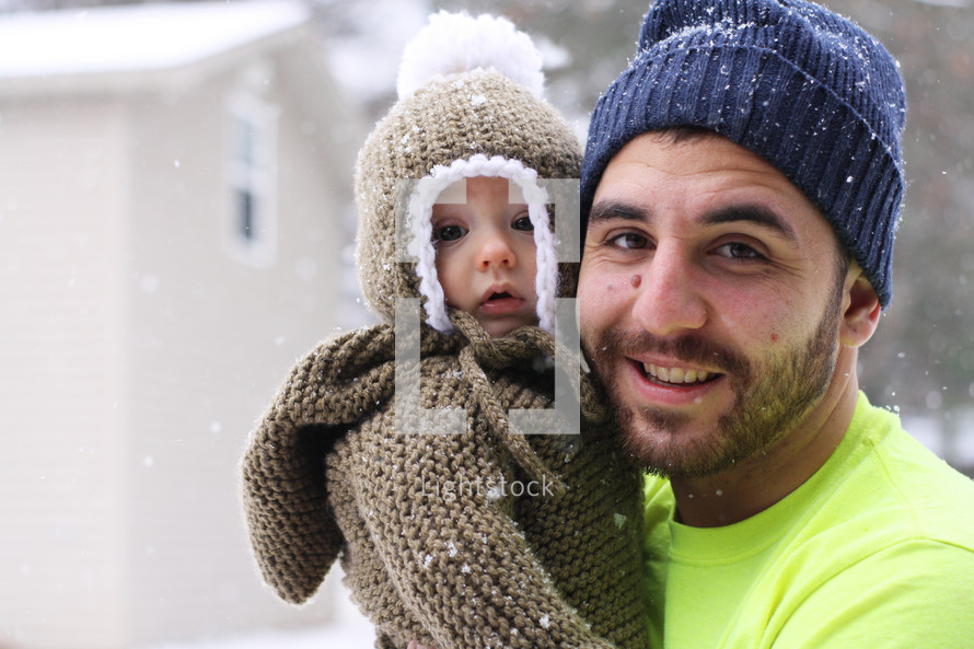 father holding an infant outdoors in snow 