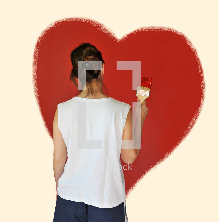 Woman painting a red heart on a wall.
