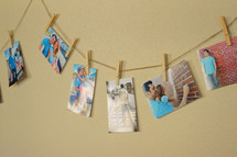 Snapshots of people, clothes pinned to a string on a wall