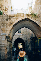 woman in a hat walking under an arched walkway 