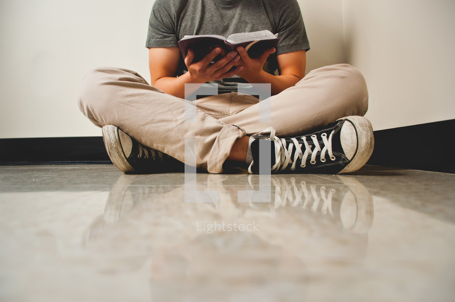 a man sitting on the floor reading a Bible 