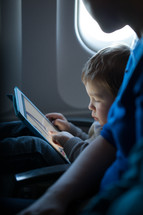 Little boy playing with a tablet in an airplane