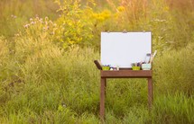 easel, art supplies, and a blank canvas outside 