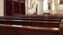 Slow-motion dramatic shot of empty wooden church pews with columns in the background.