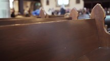 Slow-motion dramatic shot of empty wooden church pews with people in the background ready for mass to start.