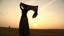 woman with a scarf dancing in the desert at sunset 