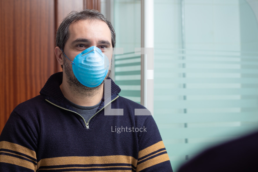 worried man with medical mask looking in the mirror