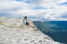 Woman sitting at the top of a mountain looking into the valley.