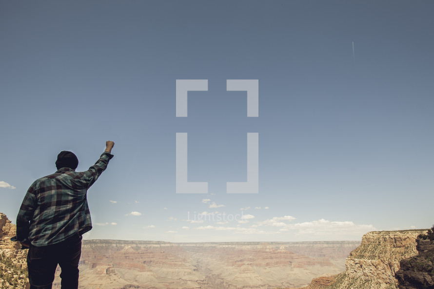 man standing looking out over the Grand Canyon with his fist in the air