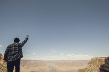man standing looking out over the Grand Canyon with his fist in the air