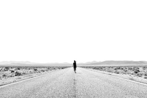 a woman walking down the middle of a desert road