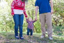 woman and man holding the hands of a toddler boy