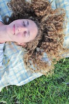 a woman napping on a blanket in the grass