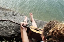a girl playing an acoustic guitar sitting on a shore 