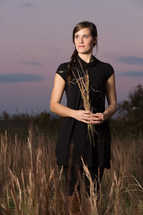 a woman standing in a field holding wheat blades
