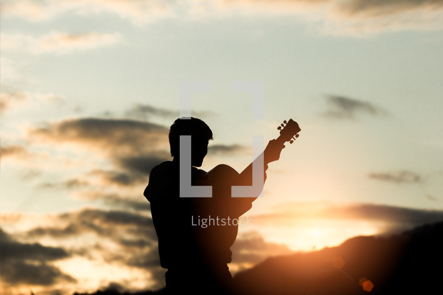silhouette of a young man playing a guitar 