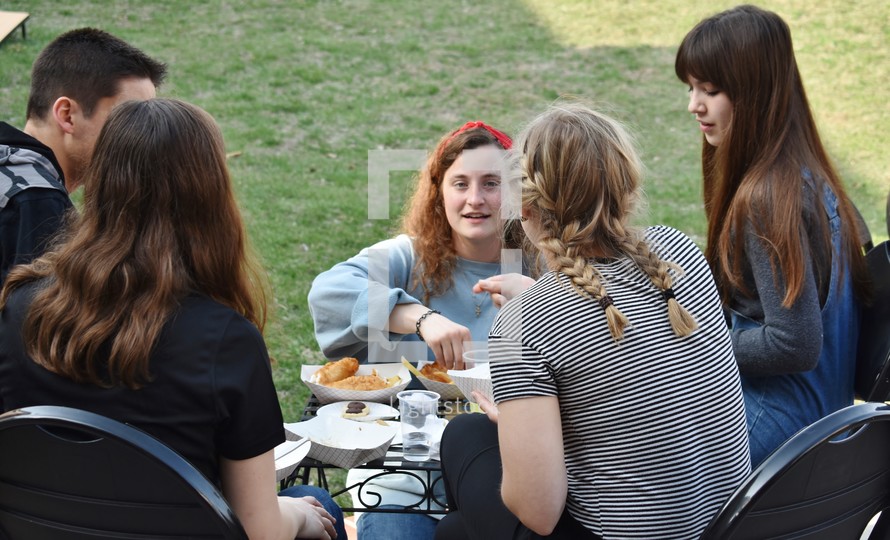 teens eating around a table outdoors 
