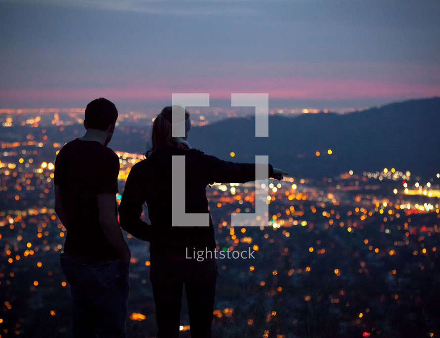 A couple standing and looking out at the lights from a suburb below