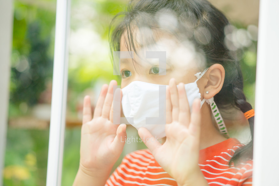child wearing a face mask behind a window 