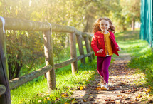 little girl walking in park on a fall day. Female toddler with yellow, red and purple clothing.