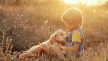 Cute little boy talking with golden retriever puppy on countryside nature background. Golden hour, sunset light. Child stroking dog. Happy lovely pet, new member of family. High quality 4k footage