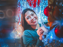 a smiling young woman decorating a Christmas tree 