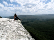 woman sitting on the edge of a cliff looking out 