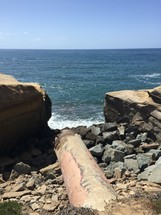 A large pipe ending at a rocky seashore.