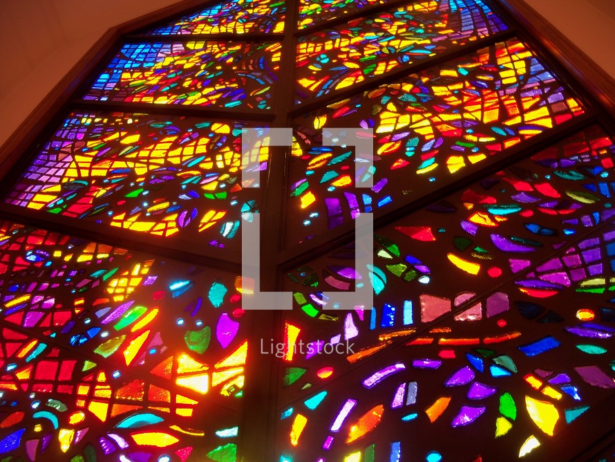 A large and colorful stained glass window lighting up a church giving the light and warmth needed to worship and feel the glow of Heaven pouring in to light up the room.