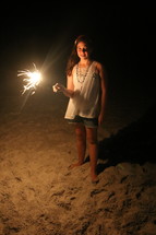a girl holding a sparkler on a beach 