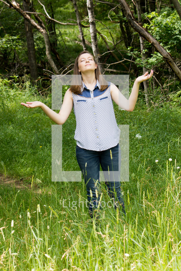 woman standing in a field with her hands in worship to God